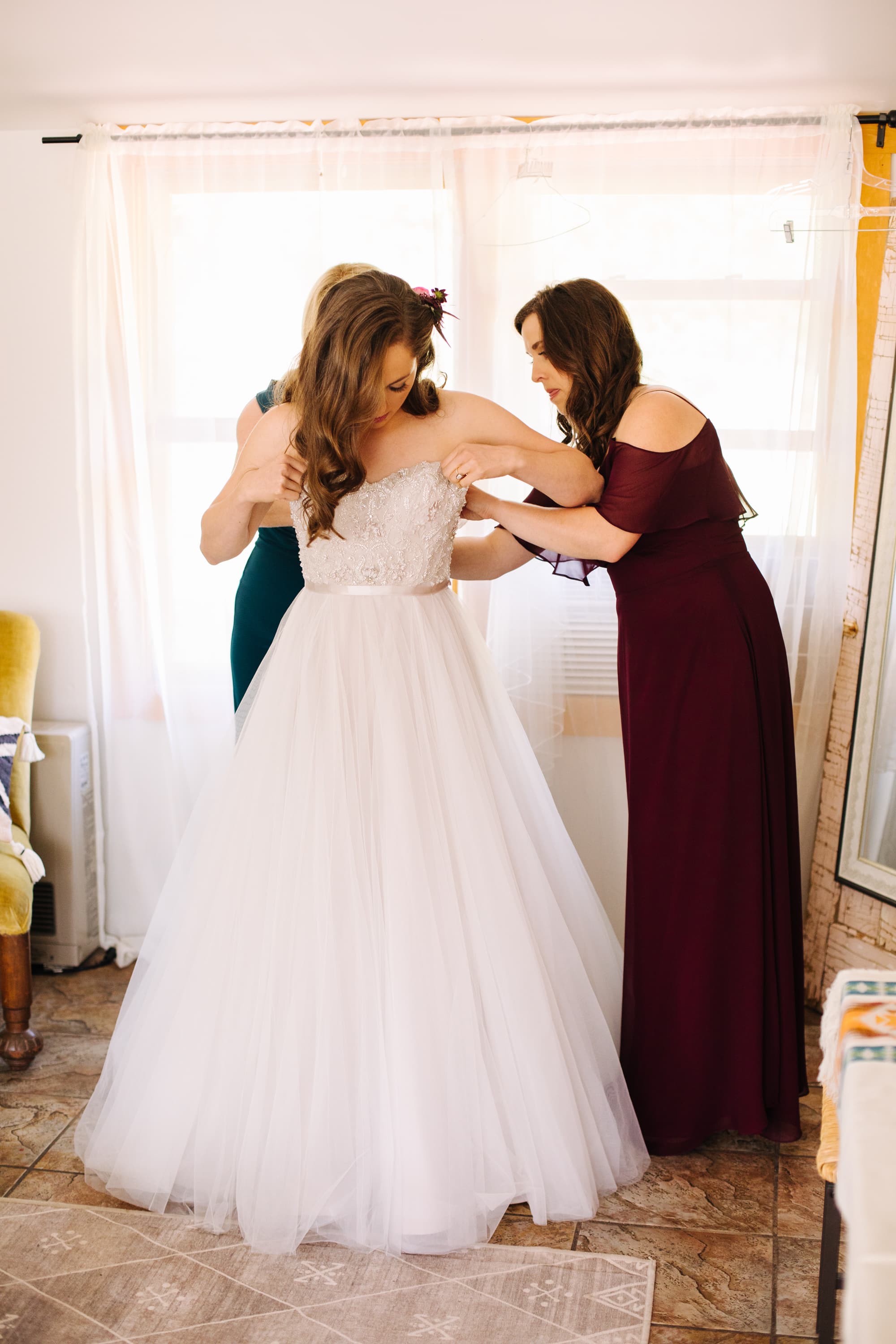 mom and sister with bride, mom with bride, getting ready bride, wedding getting ready, bride putting on dress, burgundy maid of honor dress, tule skirt wedding dress