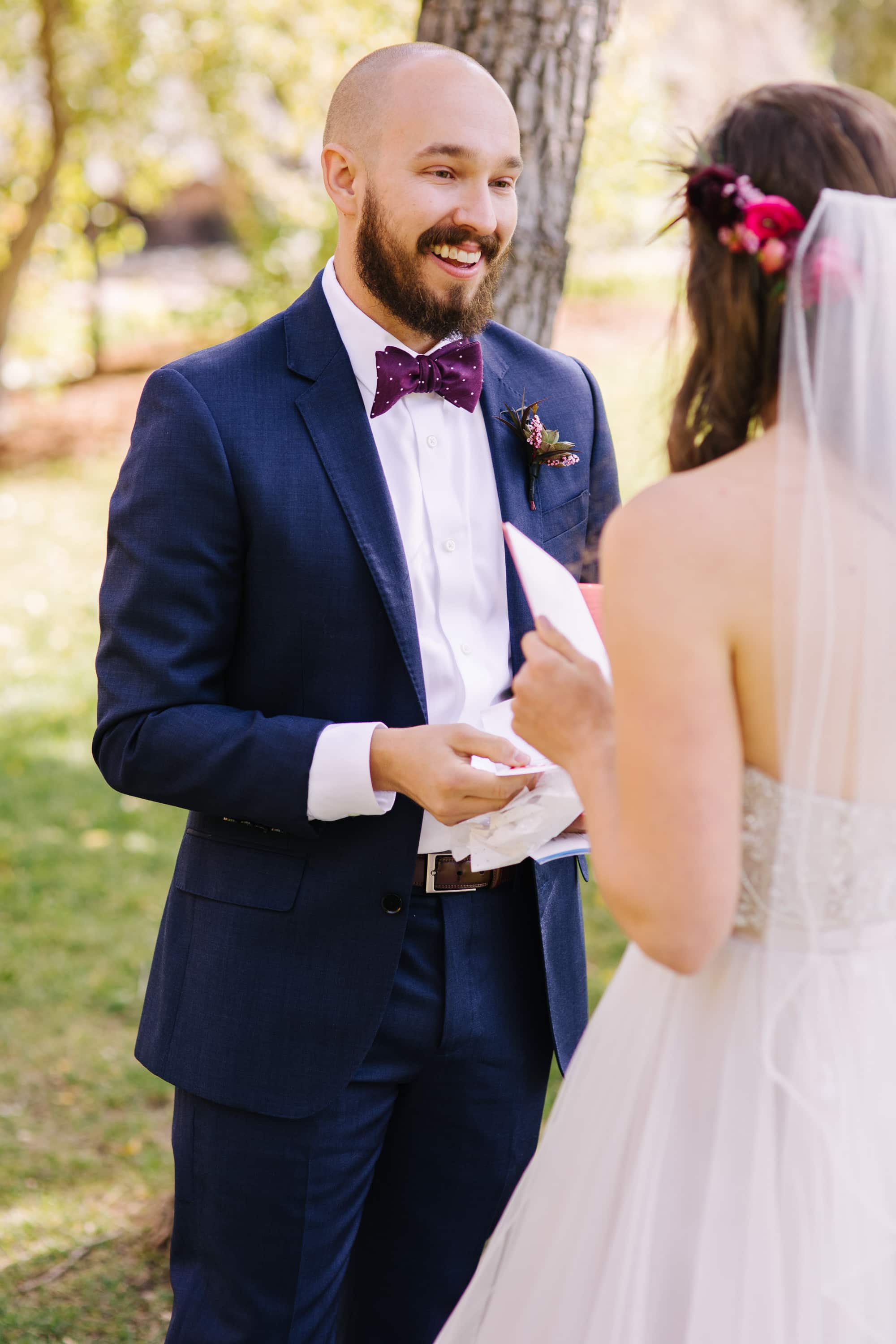 bride and groom exchanging gifts, bride and groom reading letters, outdoor wedding, colorado wedding photographer, bride with veil, blue suit groom, maroon bow tie, planet bluegrass wedding, planet bluegrass, lyons colorado wedding