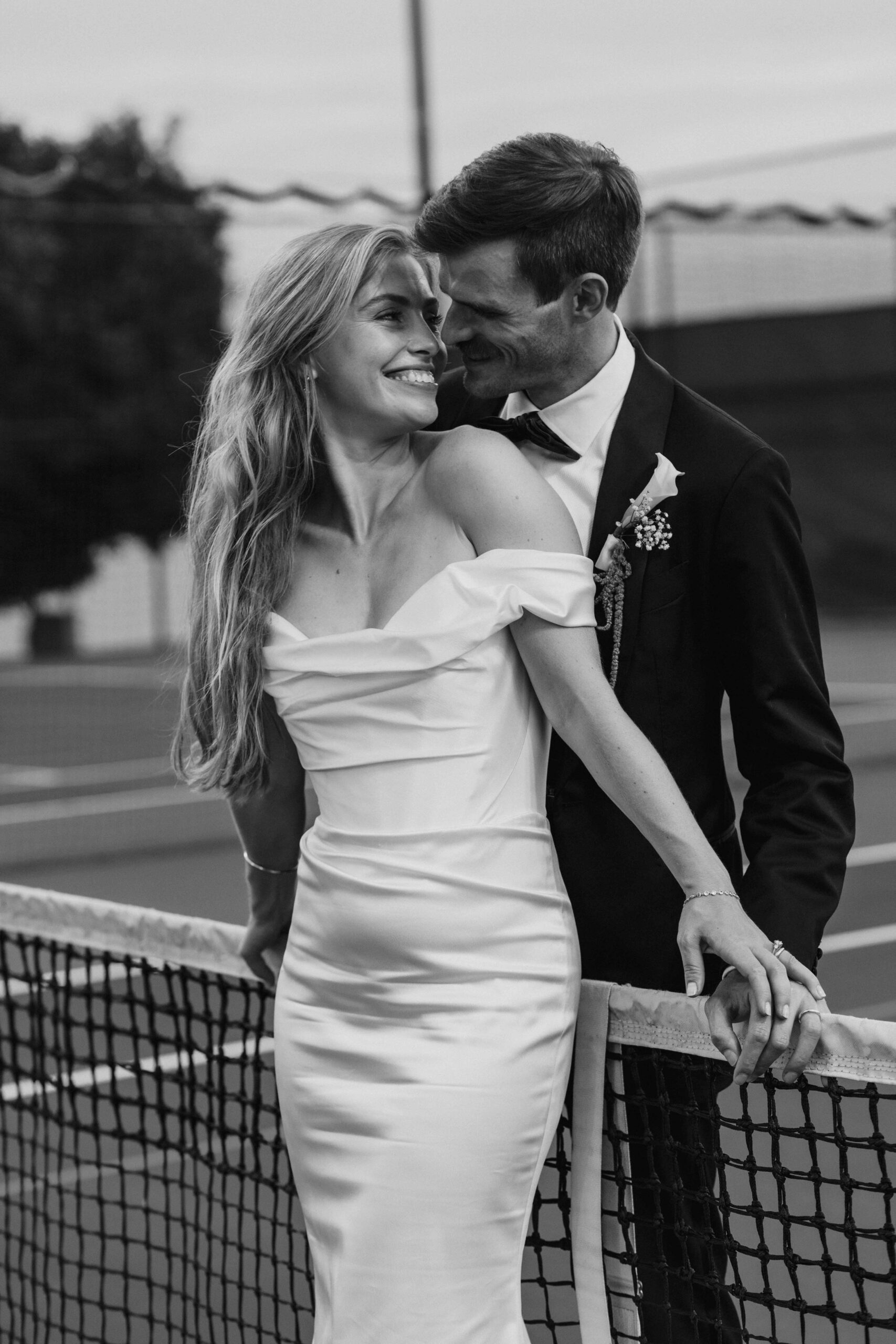 Black and white film photo of bride and groom snuggling on the tennis court during Seattle Tennis club wedding shot by Seattle wedding photographer, Erin Witt