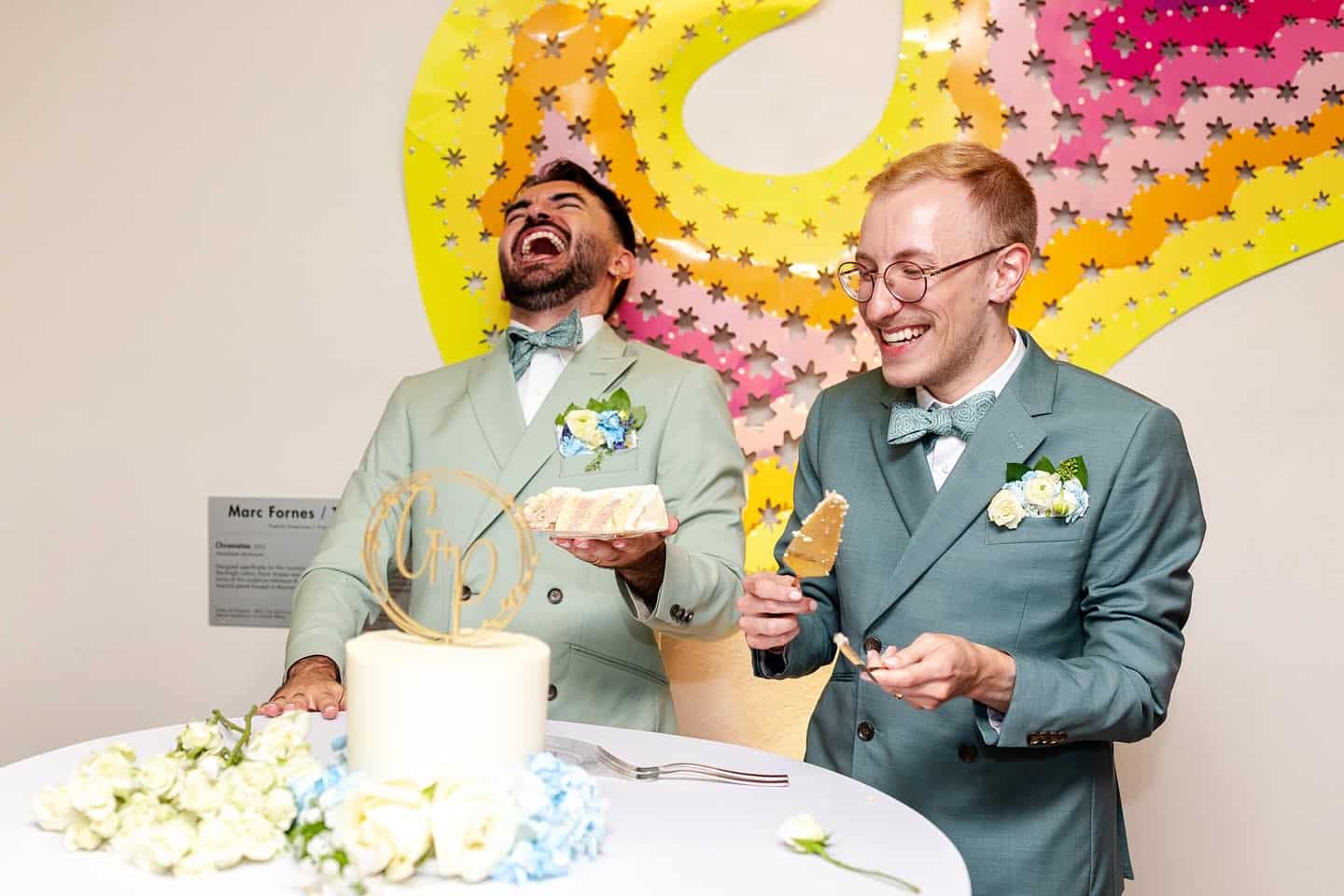 Both grooms laughing during cake cutting at the Denver Botanic Gardens during their downtown Denver LGBTQ wedding.
