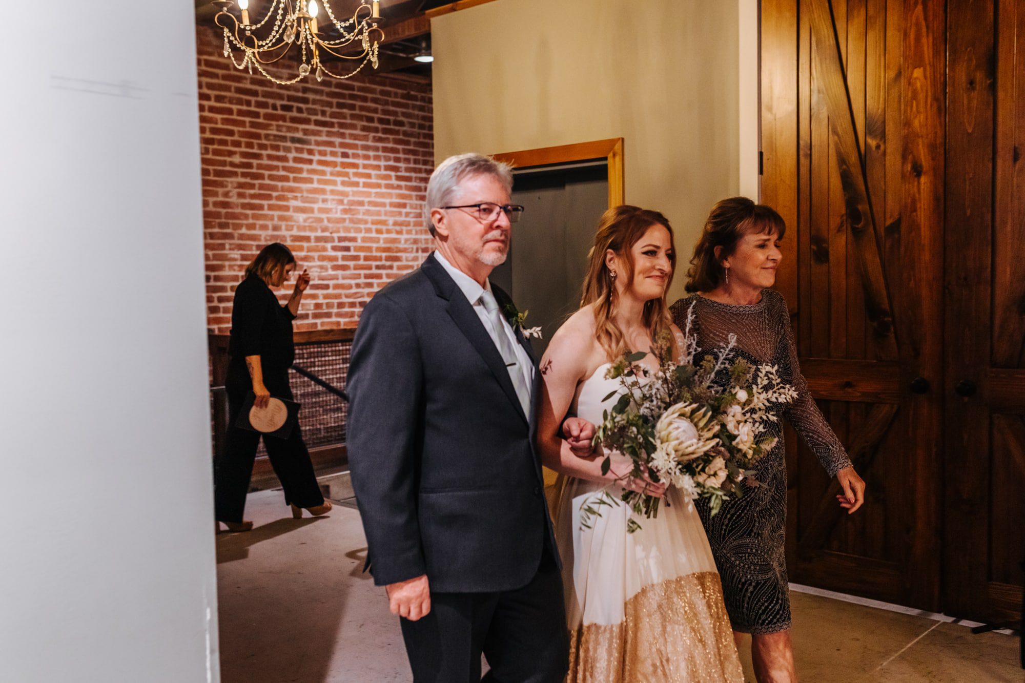 st vrain wedding venue, st vrain wedding, longmont wedding venue, industrial wedding venue, colorado wedding photographer, indoor wedding ceremony, bride walking down aisle with both parents, bride with mom and dad