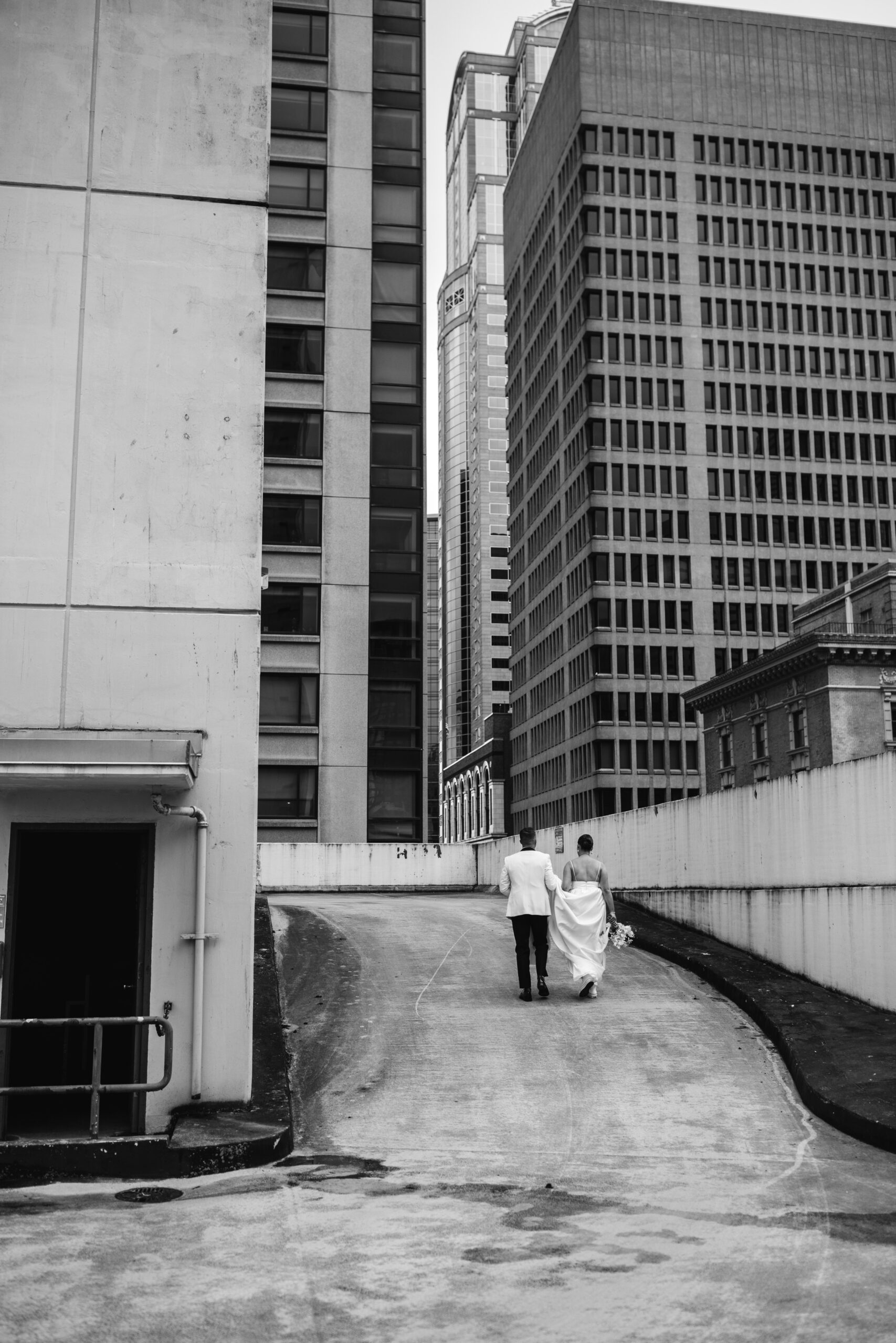 Black and white photo of bride and groom, walking together on top of a parking garage in downtown Seattle before their black tie wedding at the Seattle Art Museum