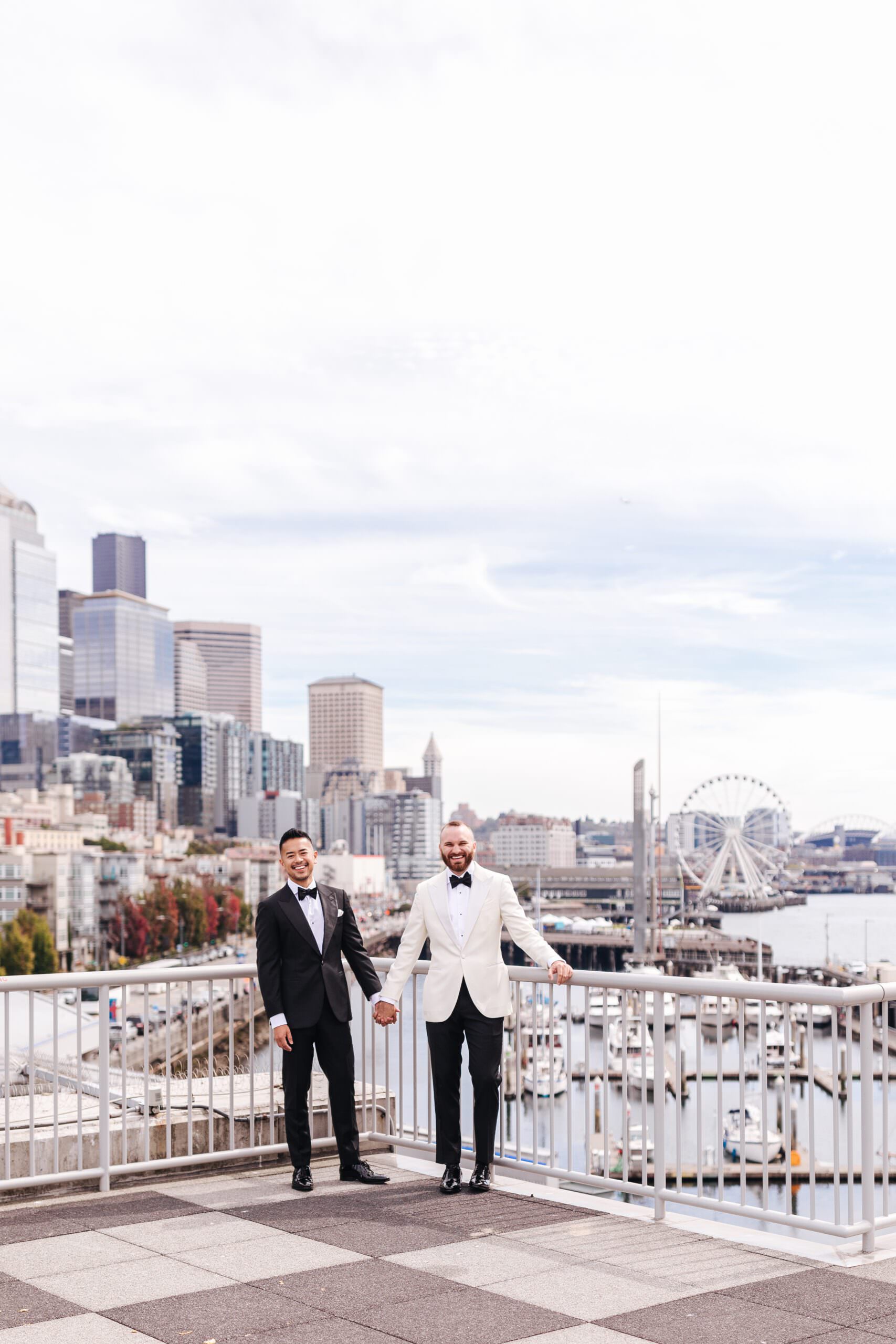 Two grooms at Bell Harbor Convention Center overlooking Elliott Bay in downtown Seattle before their urban city LGBTQ wedding.