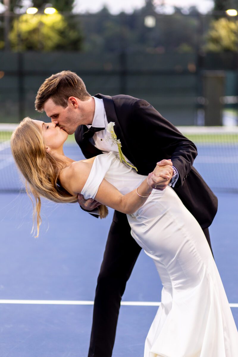 Bride and groom during portraits on the tennis court of Seattle Tennis Club, dip kiss