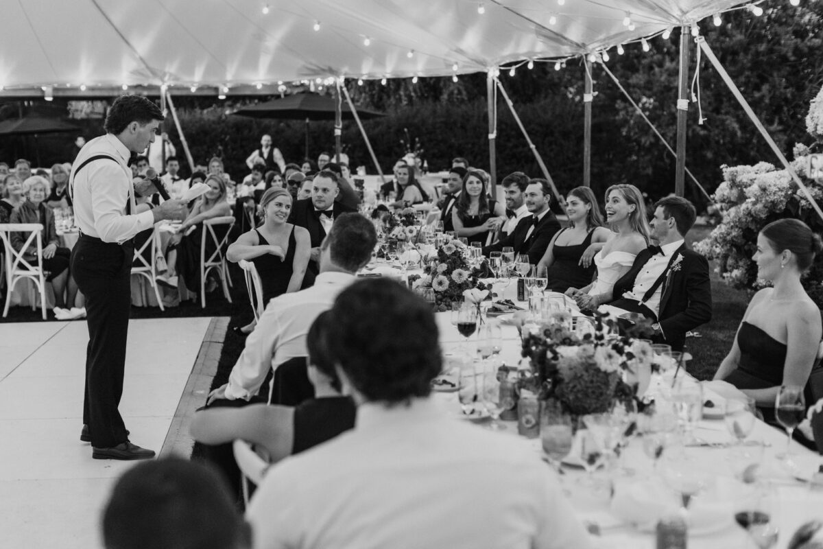 Black and white photo of best man giving speech under tent at Seattle wedding reception