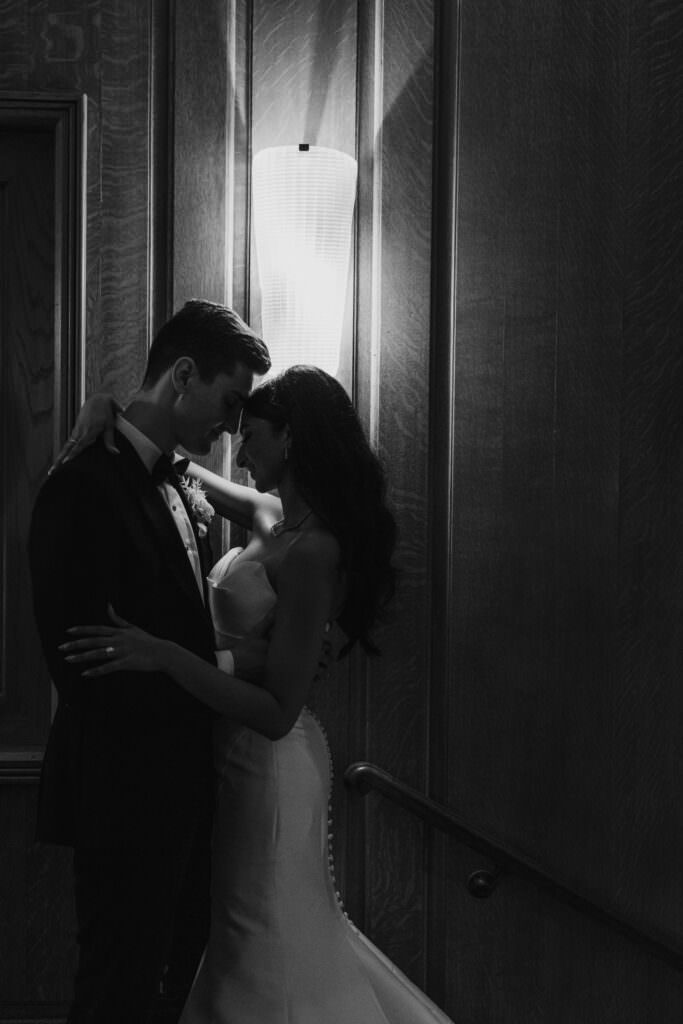 Bride and groom embracing in front of light in moody intimate photo