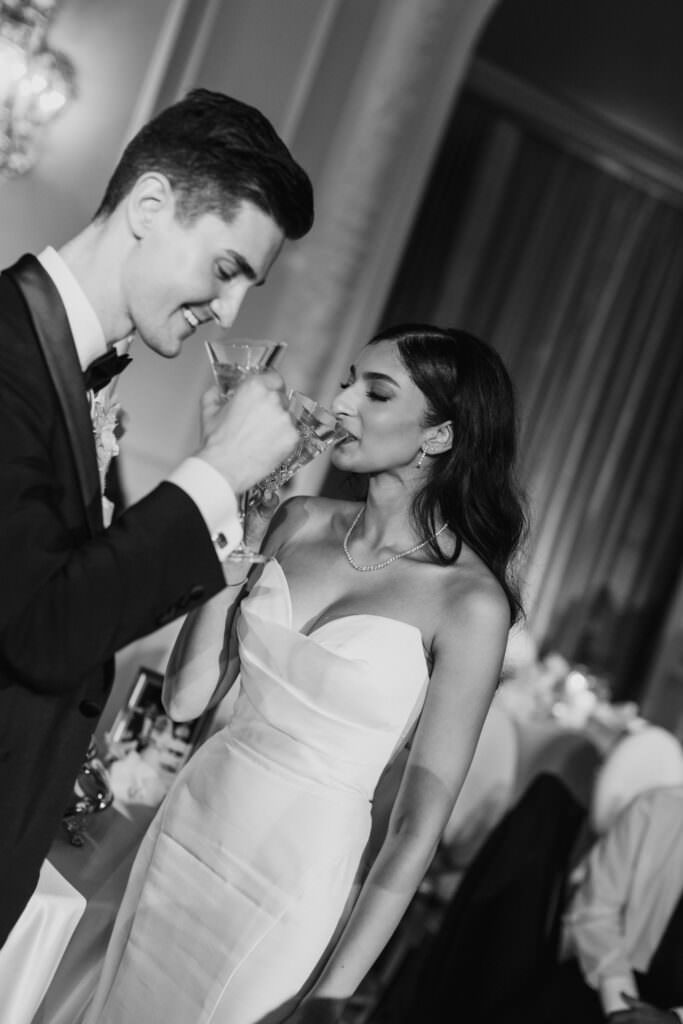 Black and white photo of bride and groom sipping champagne after cutting the cake