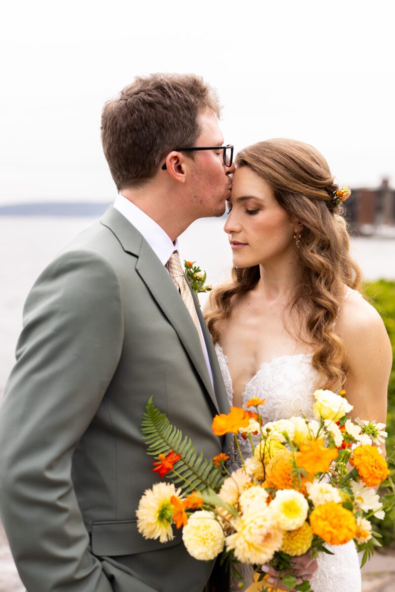Bride and groom Portraits on Lake Washington at the Woodmark hotel and still spot in Kirkland. Groom, sage, green suit, yellow, and orange wedding flowers.