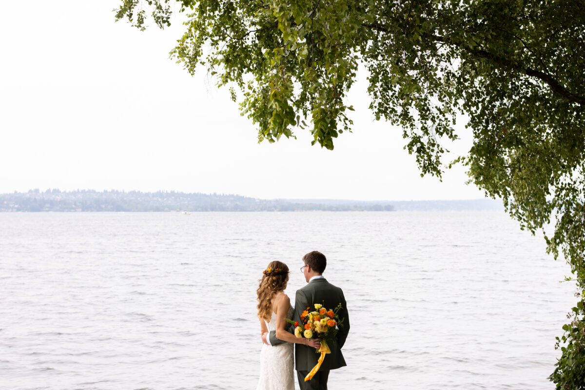 Bride and groom Portraits on Lake Washington at the Woodmark hotel and still spot in Kirkland. Groom, sage, green suit, yellow, and orange wedding flowers.