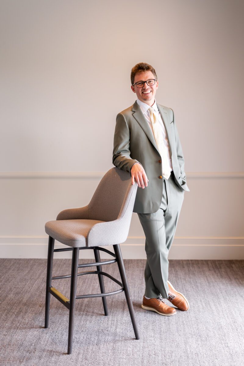 Groom in light green suit posing with chair for grooms Portraits ahead of his Seattle wedding
