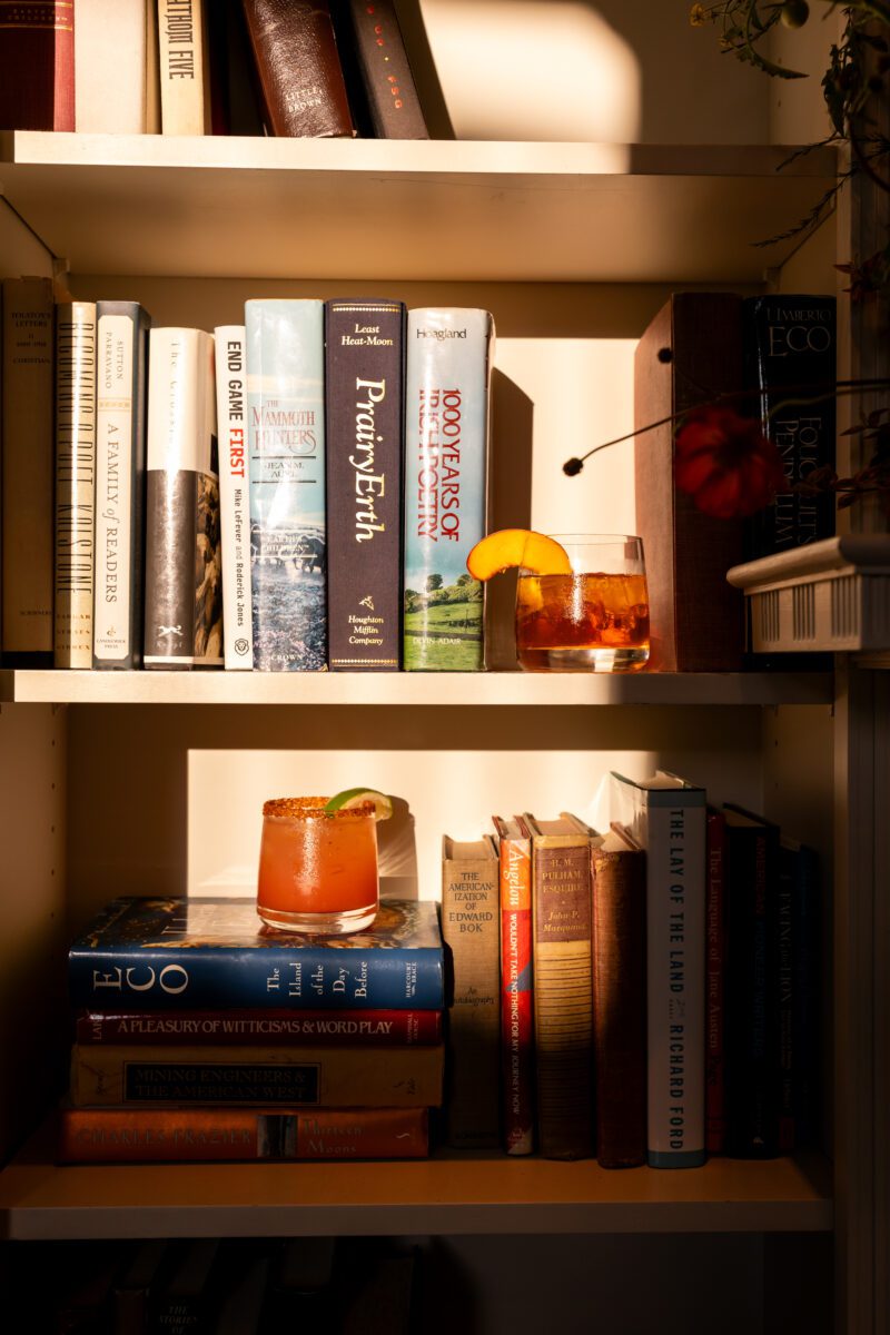Close-up photo of bride and groom signature cocktails during sunset with books from library at the Woodmark Hotel