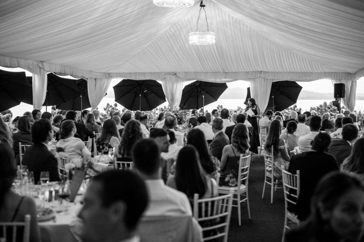 Black and white photo of friend giving speech under tent at Woodmark hotel wedding