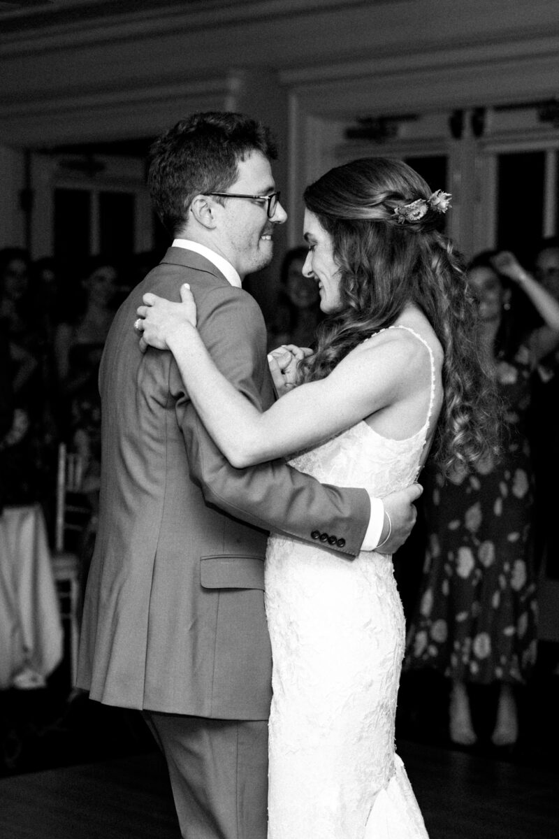 Black-and-white photo of Bride and groom having first dance while guests look on