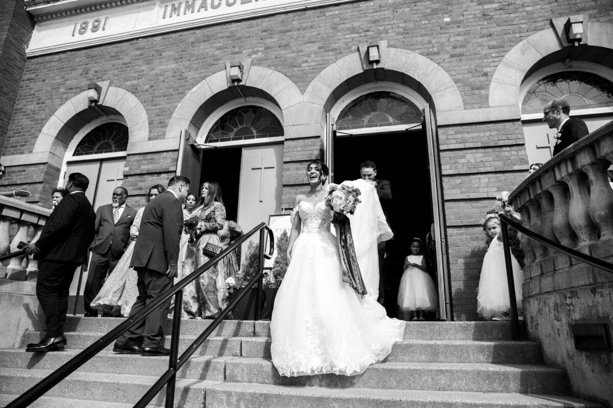 Bride and groom walking out of church with groom carrying bride's dress