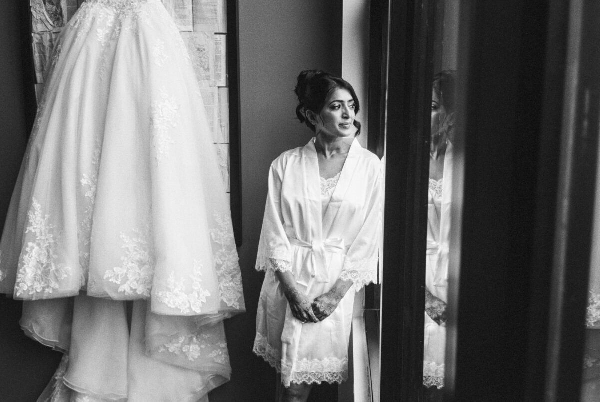 Bride looking out window with wedding dress behind her