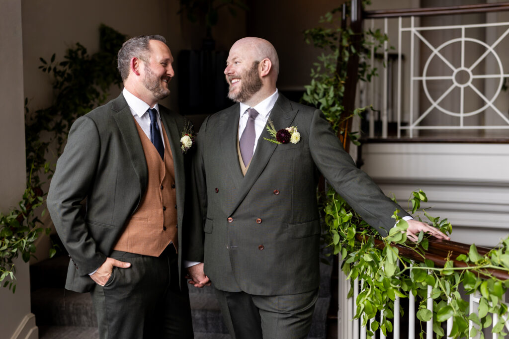 Two grooms holding hands smiling at each other before Woodmark Hotel reception